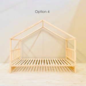 May include: A wooden bed frame with a house-shaped canopy. The frame is made of natural wood and has a slatted headboard and footboard. The canopy is made of two pieces of wood that meet at a point in the center. The bed frame is sitting on a light wood floor.