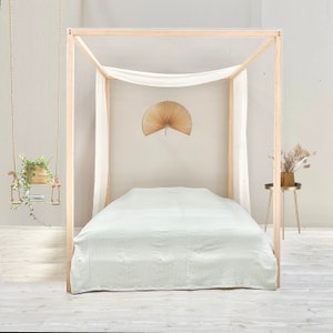 May include: A light green linen bed sheet on a wooden bed frame with a white canopy. The bed is in a room with white walls and a wooden floor.