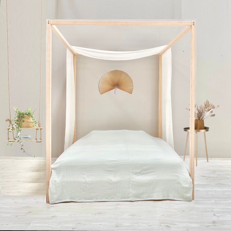 May include: A light green linen bed sheet on a wooden bed frame with a white canopy. The bed is in a room with white walls and a wooden floor.