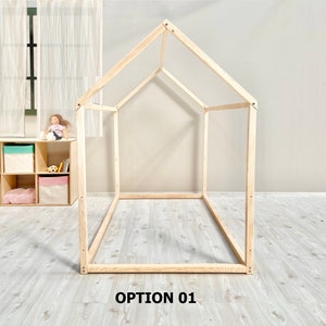 May include: A wooden frame for a bed in the shape of a house. The frame is made of natural wood and is unfinished. The frame is sitting on a light wood floor. The text "OPTION 01" is printed below the frame.