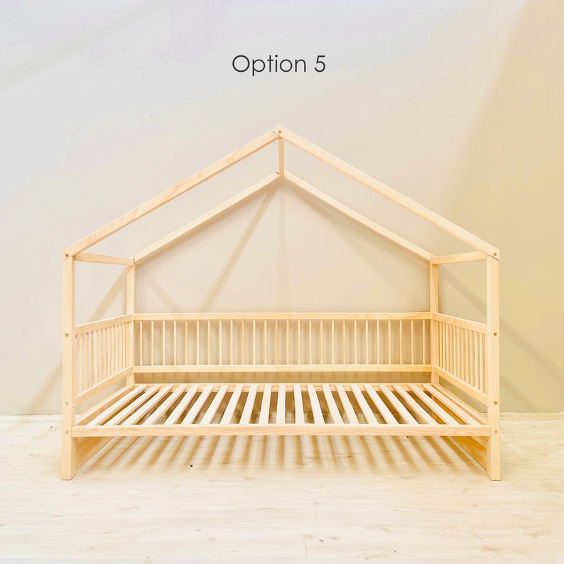 May include: A wooden bed frame with a house-shaped canopy. The bed frame is made of natural wood and has a slatted headboard and footboard. The canopy is made of two pieces of wood that meet at a point in the center. The bed frame is sitting on a light wood floor.