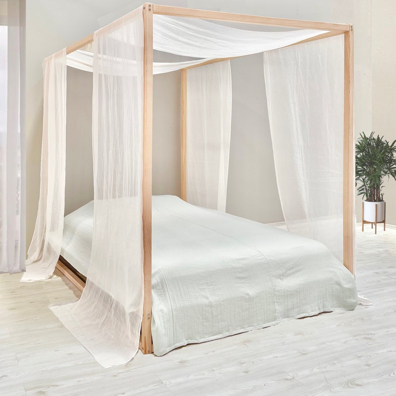 May include: A wooden canopy bed frame with white sheer curtains. The bed is made with a light green bedspread.