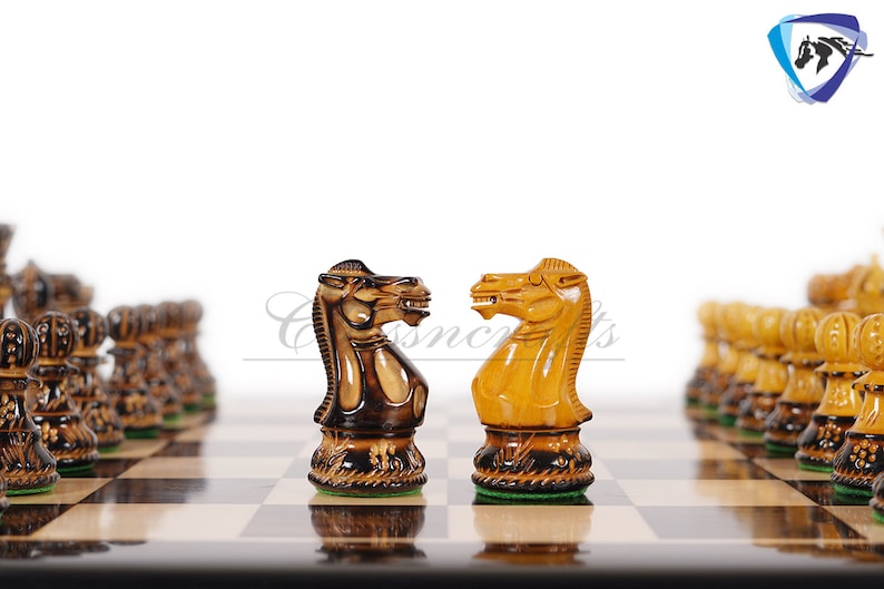 Pu&ograve; includere: Due cavalieri degli scacchi in legno si fronteggiano su una scacchiera. Il cavaliere a sinistra &egrave; marrone scuro e il cavaliere a destra &egrave; marrone chiaro. La scacchiera &egrave; in legno con caselle chiare e scure alternate.