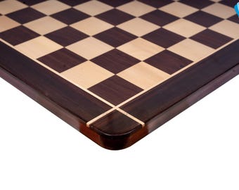 May include: Close-up of the corner of a wooden chessboard with a dark brown border and light brown squares.