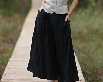 May include: A black linen maxi skirt with a flowing silhouette. The skirt is worn with a light gray vest.