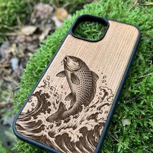 Può includere: Custodia per telefono in legno con bordo nero. Il design presenta un'incisione dettagliata di un pesce che salta dalle onde. Il pesce e le onde sono marrone scuro su uno sfondo chiaro di venature del legno.