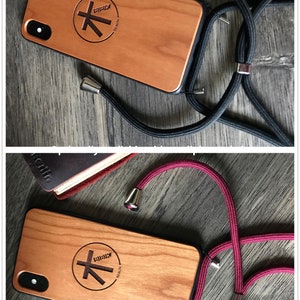 K&ouml;nnte beinhalten: Eine Holz Handyh&uuml;lle mit einer schwarzen und roten Handykette. Die H&uuml;lle hat einen schwarzen Rand und ein Logo mit der Aufschrift "BIBIK BERLIN" mit einem stilisierten Baumdesign. Die Handykette hat silberne Verschl&uuml;sse.