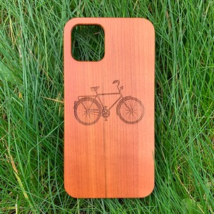 May include: A wooden phone case with a laser-engraved image of a bicycle. The case is a natural wood color.