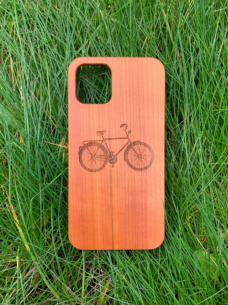 May include: A wooden phone case with a laser-engraved image of a bicycle. The case is a natural wood color.