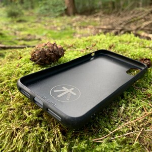 May include: Black phone case with a raised circle logo that says "Albero" in white text. The case is lying on a bed of green moss.