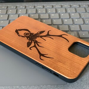May include: A wooden phone case with a laser-engraved stag design. The case is brown with a black border and a cutout for the phone's camera.