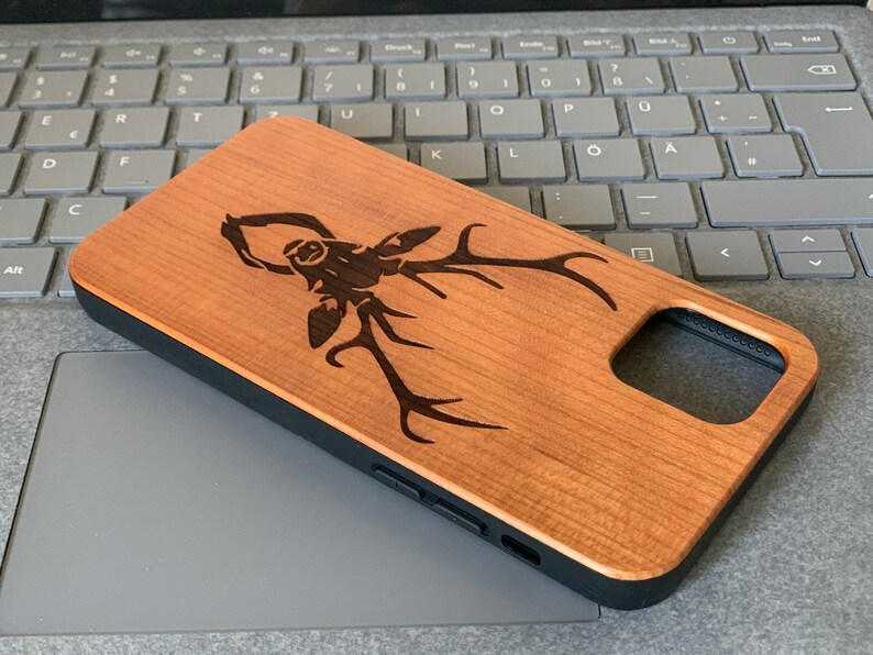 May include: A wooden phone case with a laser-engraved stag design. The case is brown with a black border and a cutout for the phone's camera.