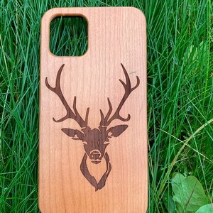 May include: A wooden phone case with a laser-engraved deer head design. The case is a light brown color and has a natural wood grain.