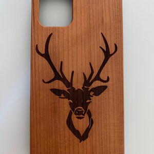 May include: A wooden phone case with a laser-engraved deer head design. The case is a light brown color and has a cutout for the phone's camera.