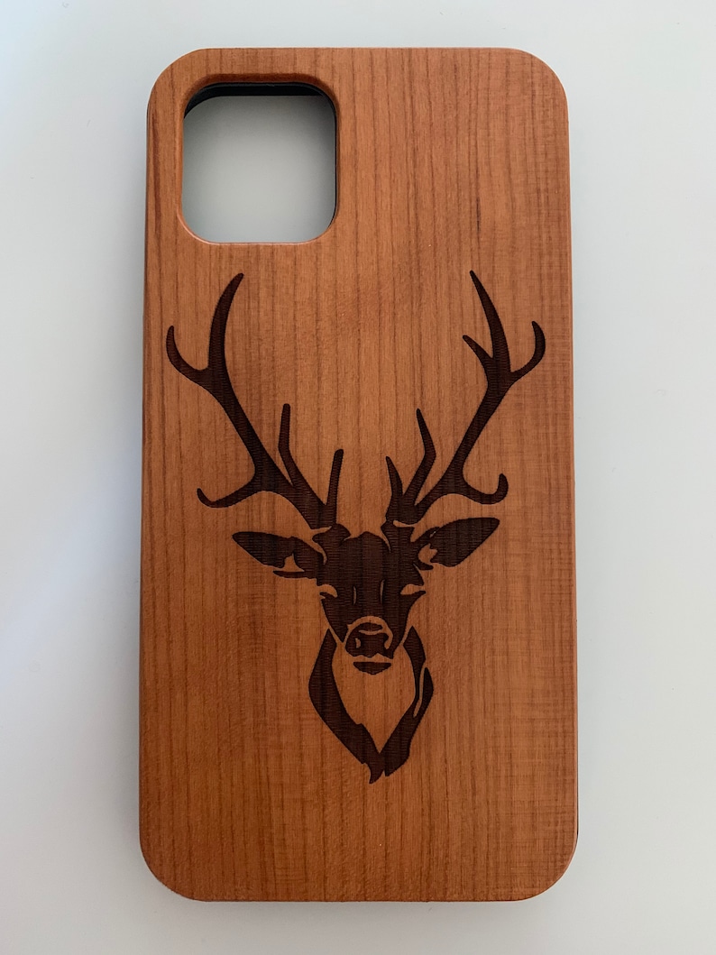 May include: A wooden phone case with a laser-engraved deer head design. The case is a light brown color and has a cutout for the phone's camera.