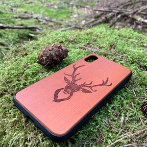 May include: A brown wooden phone case with a laser-engraved deer design. The case has a black rubber bumper.