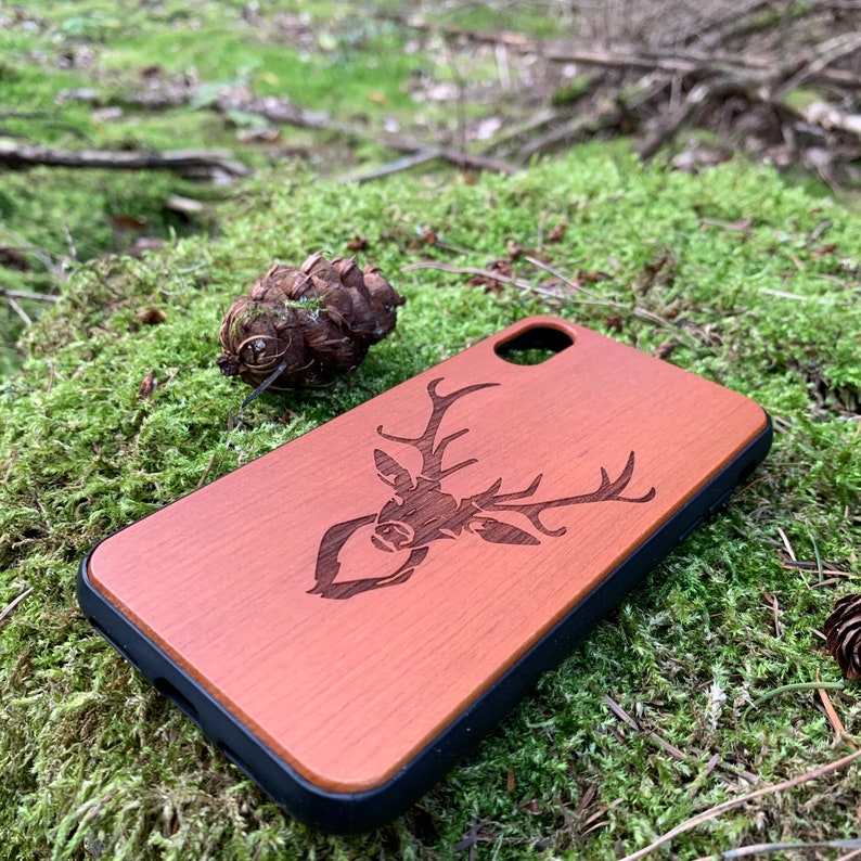 May include: A brown wooden phone case with a laser-engraved deer design. The case has a black rubber bumper.