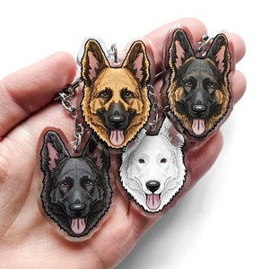 May include: Three German Shepherd dog keychains. The keychains are made of clear acrylic and feature a black and white German Shepherd, a brown and white German Shepherd, and a white German Shepherd.