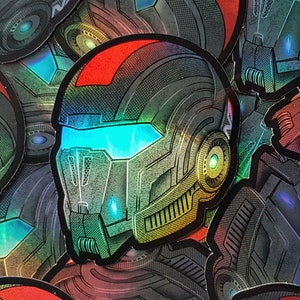 Pode incluir: Uma cole&ccedil;&atilde;o de autocolantes hologr&aacute;ficos com um design de capacete futurista. O capacete &eacute; predominantemente cinzento com detalhes vermelhos e uma viseira azul brilhante. Os autocolantes t&ecirc;m um acabamento met&aacute;lico iridescente, refletindo v&aacute;rias cores.