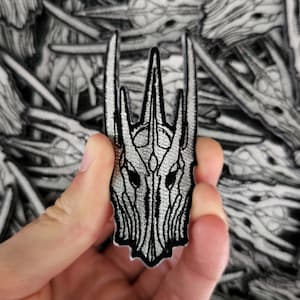 Peut inclure: Un patch brodé argenté et noir représentant l'Anneau Unique du Seigneur des Anneaux. Le patch présente un design détaillé de l'inscription de l'anneau et l'inscription "Un anneau pour les gouverner tous, Un anneau pour les trouver, Un anneau pour les amener tous, et dans les ténèbres les lier."