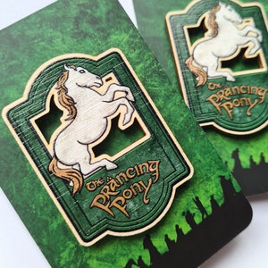 May include: A wooden sign with a green background and gold lettering that reads "The Prancing Pony". A white horse with a brown mane is depicted in the centre of the sign, rearing up on its hind legs.