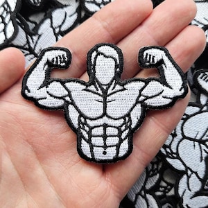 May include: A black and white embroidered patch featuring a stylized figure with a muscular physique, defined abdominal muscles, and arms raised in a flexing pose. The design is outlined in black thread with white fill, showcasing a detailed torso.