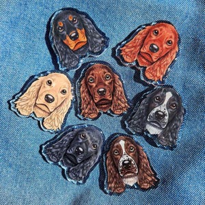 May include: Seven different dog breed illustrations printed on clear acrylic. The dogs are all facing forward and have different colored fur. The illustrations are in a circular arrangement.