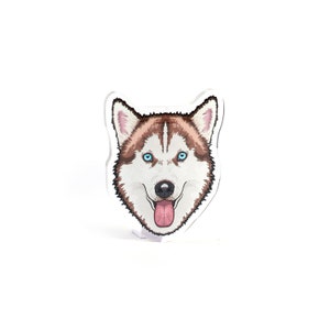 May include: A white and brown husky dog with blue eyes and a pink tongue sticking out. The dog's head is illustrated in a cartoon style and is printed on a clear acrylic plaque.