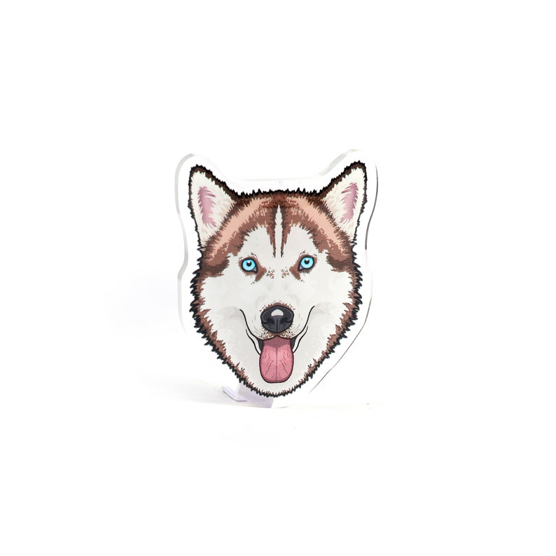 May include: A white and brown husky dog with blue eyes and a pink tongue sticking out. The dog's head is illustrated in a cartoon style and is printed on a clear acrylic plaque.