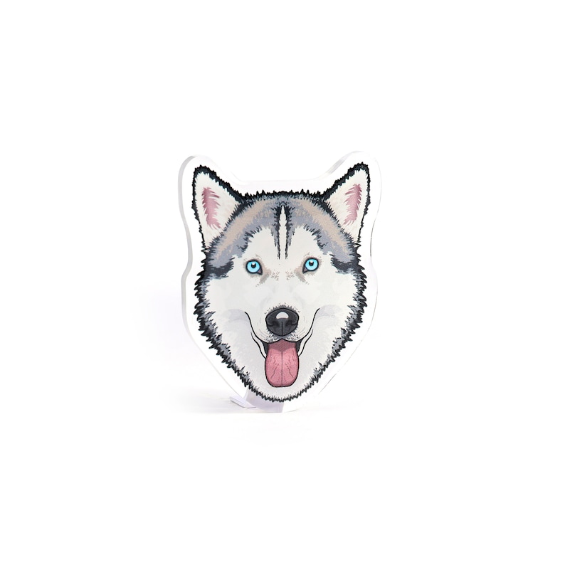 May include: A sticker featuring a cartoon husky dog with blue eyes and a pink tongue sticking out. The dog is looking directly at the viewer.