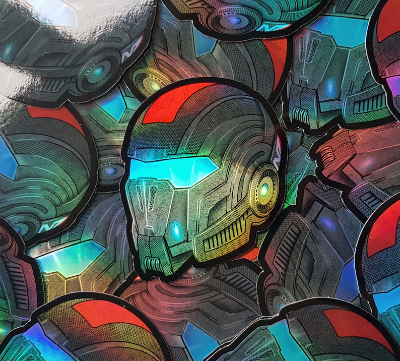 Pode incluir: Uma cole&ccedil;&atilde;o de autocolantes hologr&aacute;ficos com um design de capacete futurista. O capacete &eacute; predominantemente cinzento com detalhes vermelhos e uma viseira azul brilhante. Os autocolantes t&ecirc;m um acabamento met&aacute;lico iridescente, refletindo v&aacute;rias cores.
