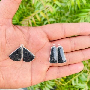 Op de afbeelding: Vier zwarte stenen hangers in zilveren monturen. Twee hangers zijn waaiervormig en twee zijn trapeziumvormig. Elk stuk is voorzien van een klein zilveren oogje aan de bovenkant en toont een donkere, gespikkelde textuur in de gepolijste steen.