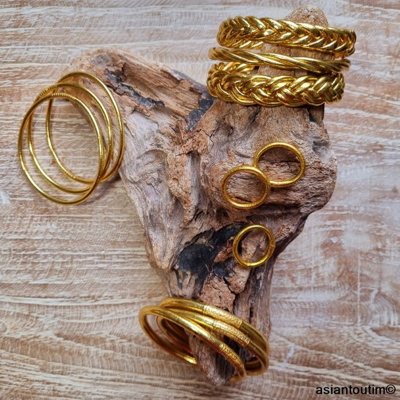 Puede incluir: Un conjunto de pulseras y anillos dorados. Las pulseras est&aacute;n apiladas una encima de la otra y tienen un dise&ntilde;o trenzado. Los anillos son simples y redondos.