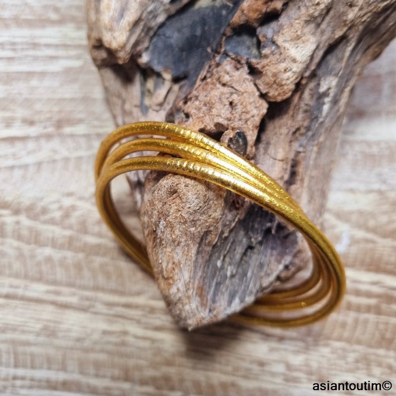 May include: Three gold-colored bangles stacked on top of each other. The bangles are smooth and shiny.