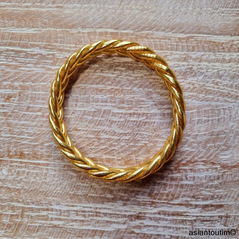 Puede incluir: Un brazalete de oro trenzado. El brazalete est&aacute; hecho de un metal grueso y trenzado y tiene un acabado liso y pulido.