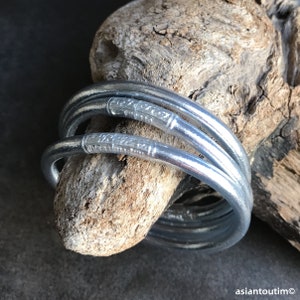 May include: Set of four silver bangles with decorative etched designs. The bangles are stacked on top of each other and are resting on a piece of driftwood.