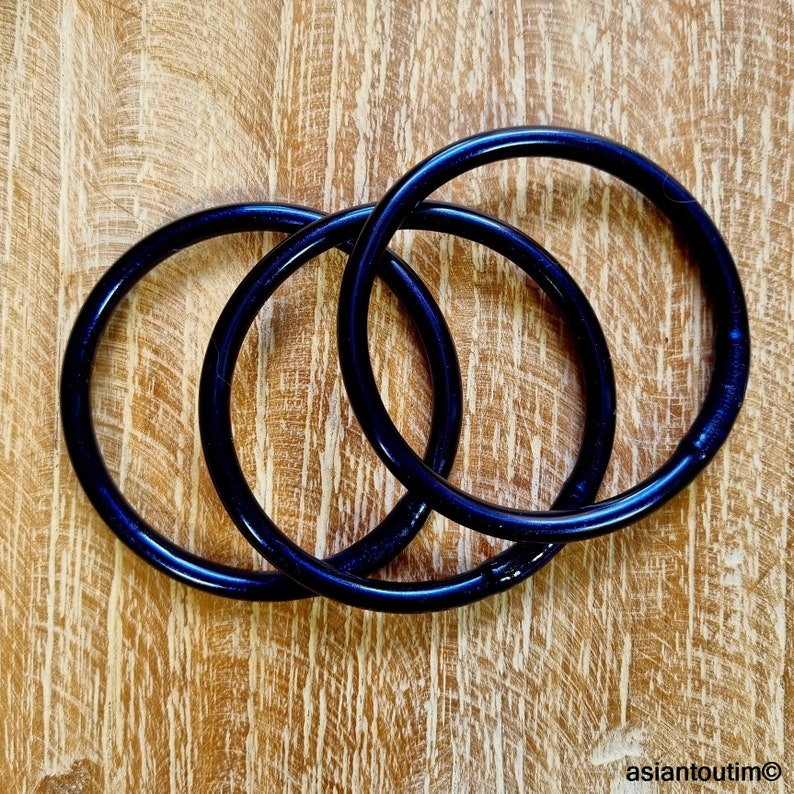 May include: Three dark blue bangles are intertwined on a light brown wooden surface. The bangles have a glossy finish and appear to be made of a solid material. The wooden surface has a natural grain pattern.
