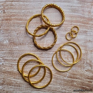 May include: A set of gold-colored bangles, some with a twisted design, arranged on a wooden surface.