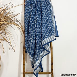 以下が含まれることがあります： 葉っぱの模様が入った青と白の綿毛布。毛布は折り畳んで木製の梯子にかけられています。