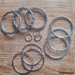 May include: A set of silver metal bangles, some with a twisted design, and some with a smooth finish. The bangles are arranged on a wooden surface.
