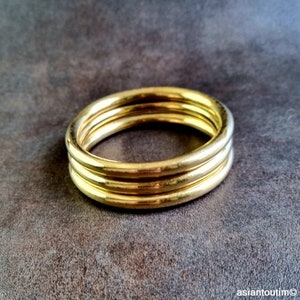 Può includere: Tre braccialetti in metallo dorati impilati uno sopra l'altro.