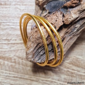May include: Three gold bangles stacked on top of each other. The bangles are smooth and shiny, with a slightly textured surface.