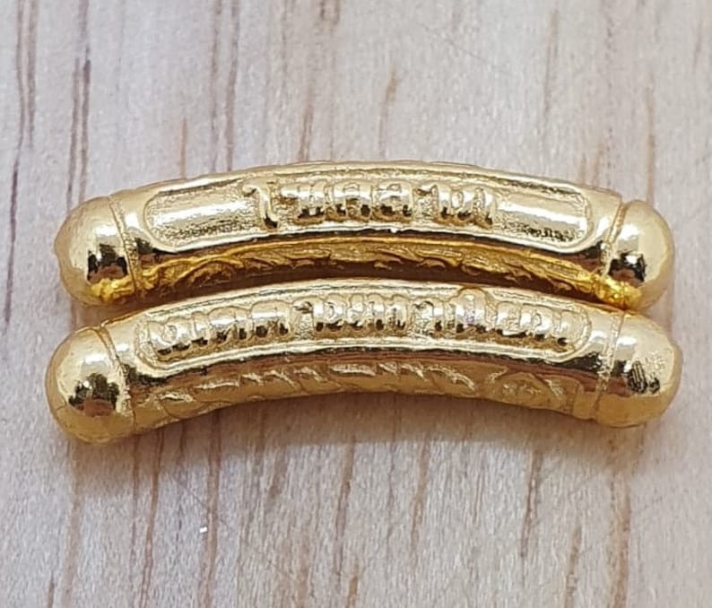 May include: Two gold-colored metal charms with intricate designs and Thai script. The charms are curved and have rounded ends.