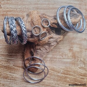 May include: A collection of silver bangles and rings. The bangles are stacked on a piece of driftwood. The rings are arranged in a circle on the wood.