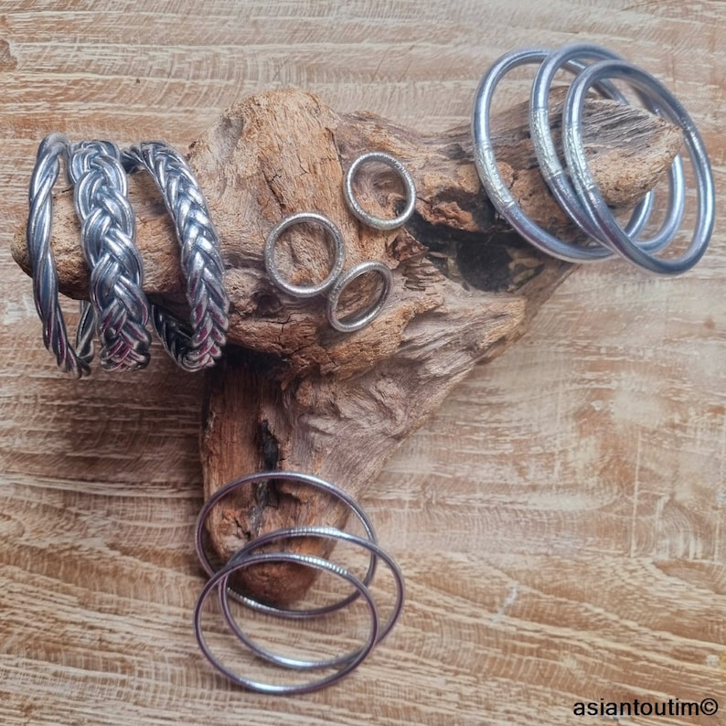 May include: A collection of silver bangles and rings. The bangles are stacked on a piece of driftwood. The rings are arranged in a circle on the wood.