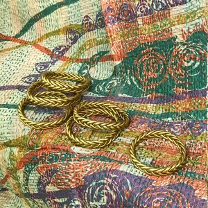 May include: A set of six gold-colored rope-style bracelets on a colorful patterned fabric background.