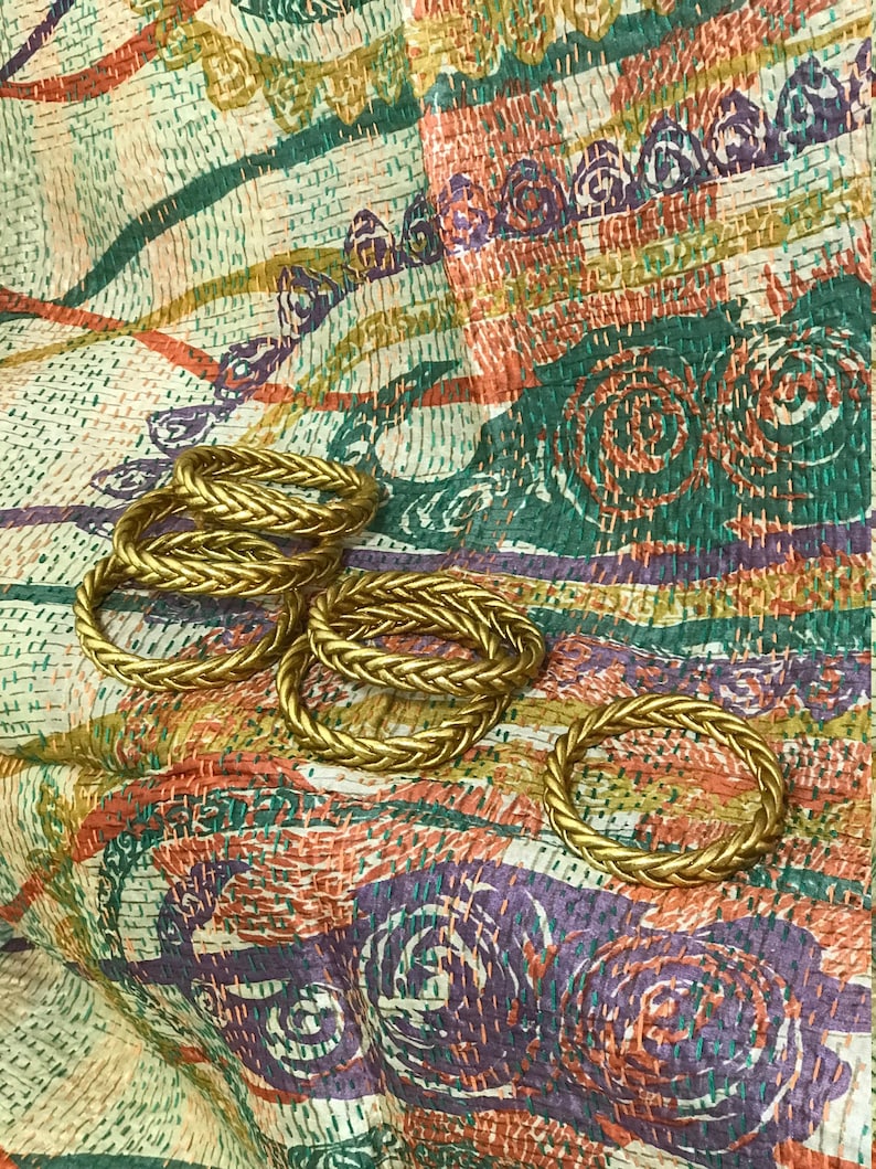 May include: A set of six gold-colored rope-style bracelets on a colorful patterned fabric background.