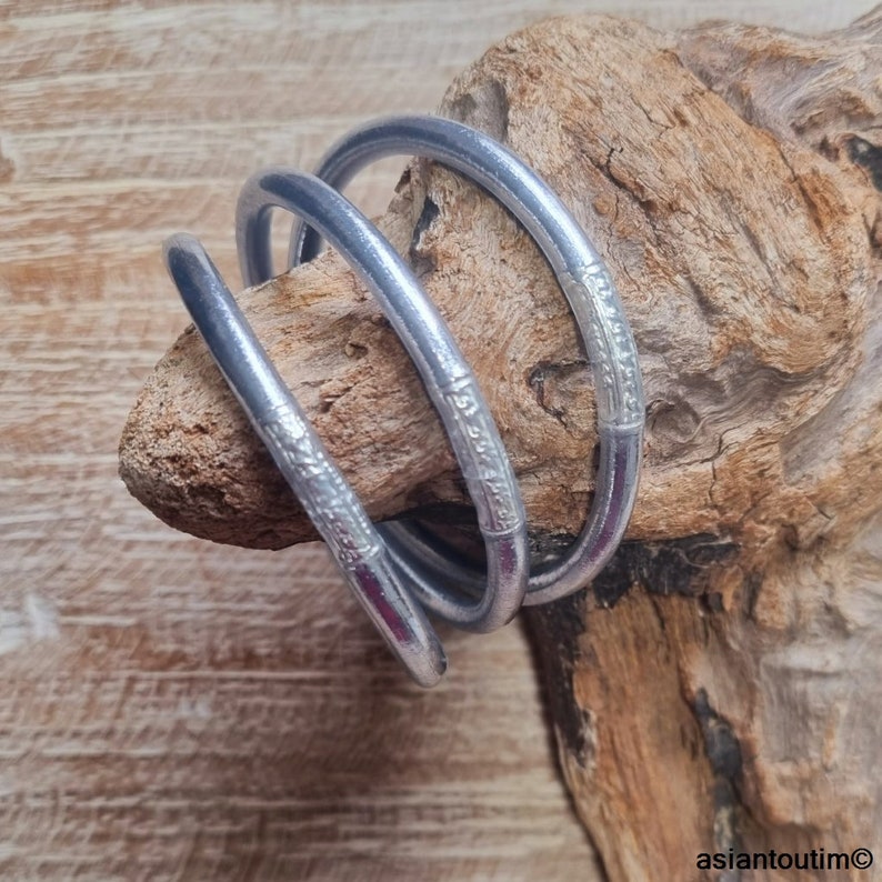 May include: Three silver bangle bracelets with an etched design. The bracelets are stacked on top of each other.