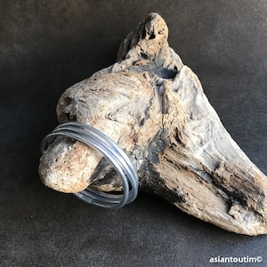 May include: Three silver metal bangles stacked on top of each other, resting on a piece of driftwood.