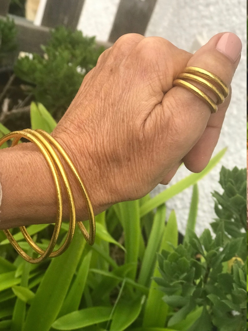 May include: A set of four gold-toned bangles worn on a person's wrist. The bangles are stacked on top of each other and are made of a smooth, shiny metal.